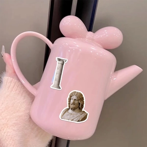 Detail of pink ceramic teapot with bow lid and Greek classical art stickers