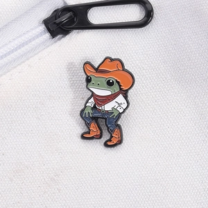 Detailed view of an enamel pin featuring a cartoon cowboy frog on a canvas bag strap
