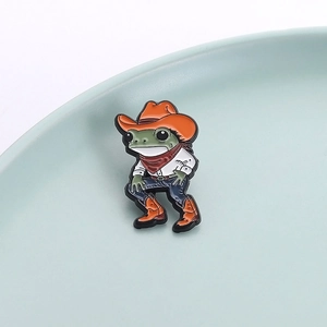 Detail of cartoon frog enamel pin in cowboy outfit placed on light blue surface