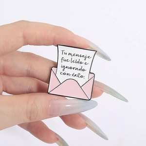 Close-up of a pink enamel letter brooch with Spanish text on white paper detail