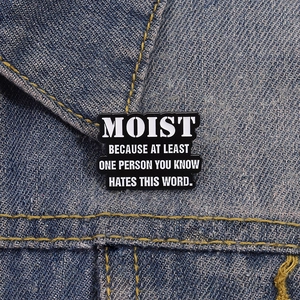 Black enamel pin with MOIST quote on blue denim jacket lapel showing product style