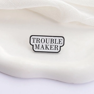 Détail de la broche en émail avec texte Trouble Maker sur fond texturé blanc élégant