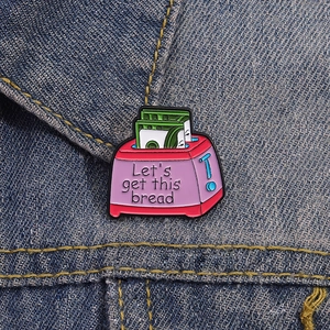 Close-up of pink toaster enamel pin with Let's get this bread text on denim jacket