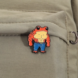 Macro shot of creative muscular frog enamel pin on a khaki canvas fabric background