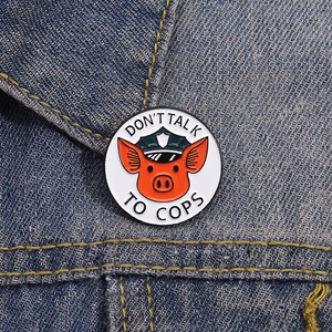 Detail of pig sheriff enamel pin with Don't Talk to Cops slogan on blue denim jacket