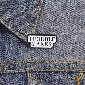 Broche en émail minimaliste Trouble Maker sur un col de veste en jean bleu foncé
