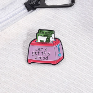 Macro detail of enamel toaster pin with Let's get this bread text on canvas bag