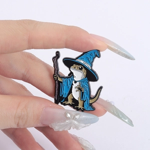 Cartoon wizard lizard enamel pin featuring blue cape and magic wand held by hand