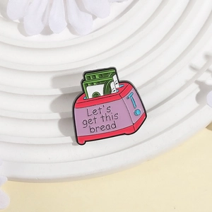 Macro detail of enamel toaster pin with Let's get this bread quote and money design