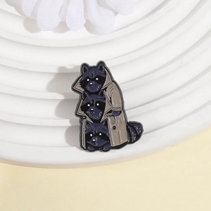 Close-up of three raccoons in a trench coat creative enamel brooch on white display