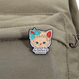 Détail d'un pin's en émail chat avec texte sur une sangle de sac à dos kaki