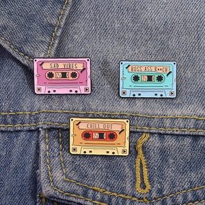Drei bunte Retro-Kassetten-Emaillenadeln auf blauem Denim-Hintergrund für Kleidung