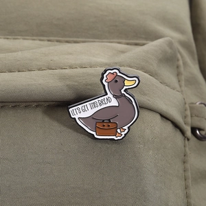 Détail du pin's canard avec texte 'LET'S GET THIS BREAD' sur un sac en toile verte