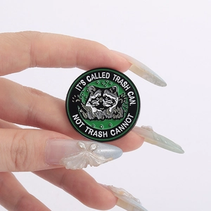 Close-up of raccoon enamel pin with 'It's called trash can not trash cannot' slogan