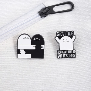 Close-up of black and white Ghost Hug enamel pins with text on canvas bag texture
