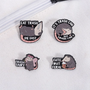 Flat lay of four funny cartoon possum enamel pins on white canvas fabric background