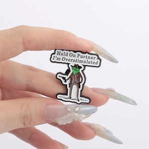 Detail shot of a green cowboy frog enamel pin with the text Hold On Partner I am Overstimulated