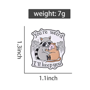 Detail of cartoon raccoon and opossum enamel pin with You're weird I'll keep you quote