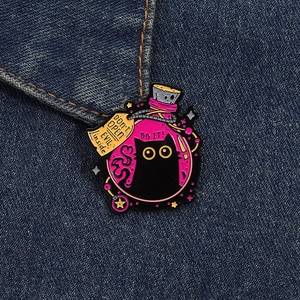 Detail of cute black cat enamel pin in a pink magic potion bottle on denim fabric