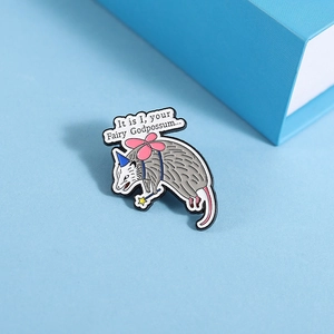 Macro detail of enamel opossum pin with wings and fairy godpossum quote on blue surface
