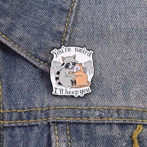 Cute enamel brooch with raccoon and opossum hugging on denim, featuring sentimental text
