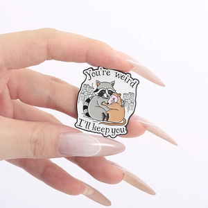 Cute cartoon enamel pin of a raccoon hugging an opossum with You're weird text
