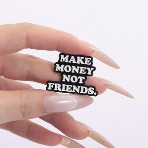 Détail de l'épingle émaillée 'MAKE MONEY NOT FRIENDS' tenue par une main élégante