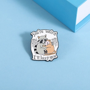 Macro shot of an enamel raccoon and opossum pin with You are weird engraving