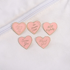 Détail macro de pin's coeur rose en émail avec bords dorés sur fond en tissu blanc
