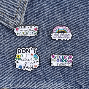 Détail de quatre épinglettes colorées en émail avec citations sur tissu denim