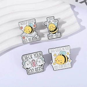 Set of four cartoon bee and ghost enamel pins displayed on a white textured stand