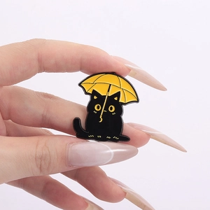Detail of cute black cat enamel pin with yellow umbrella held by hand to show size