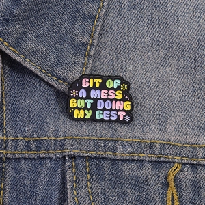 Cartoon enamel pin Bit Of A Mess But Doing My Best badge on blue denim jacket collar