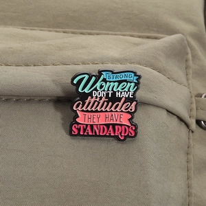 Detailed shot of an inspirational enamel pin on a green fabric backpack strap