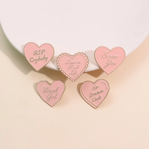 Détail des badges en émail rose en forme de cœur avec bordure dorée et slogans