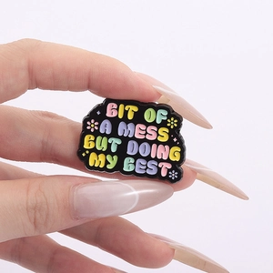 Close-up of enamel pin with 'BIT OF A MESS BUT DOING MY BEST' text and flower detail