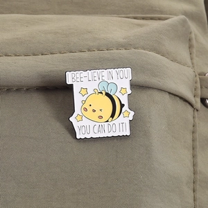 Enamel bee brooch with inspirational text pinned on a green canvas bag detail