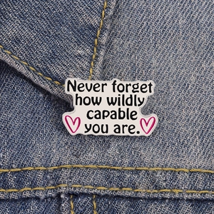 Dettaglio della spilla smaltata con citazione motivante su tessuto in denim blu