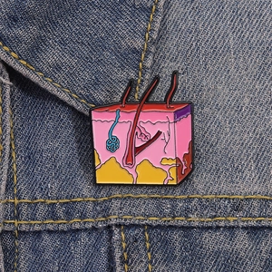 Detailed macro view of the human skin anatomy enamel pin on a dark blue denim background