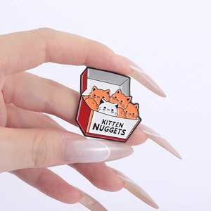Macro shot of a cartoon enamel pin featuring kitten nuggets in a red box being held