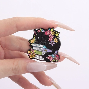 Pin's chat noir dormant sur des livres empilés avec fleurs colorées vue en gros plan