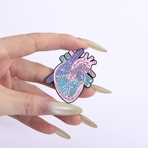 Anatomical heart enamel pin with detailed medical labeling held by a hand