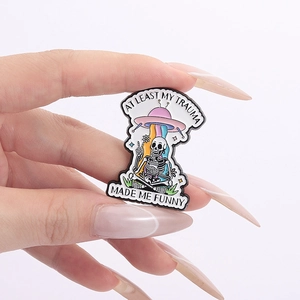 Funny cartoon skull UFO enamel pin with AT LEAST MY TRAUMA MADE ME FUNNY text for backpacks