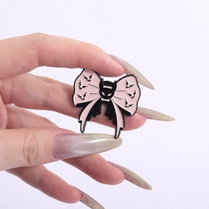 Detailed shot of pink bat bow enamel pin with gothic skull badge held in hand