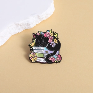 Broche en émail chat noir sur des livres avec fleurs colorées et bordure dorée