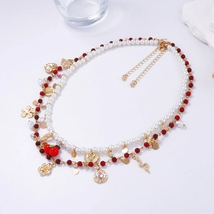 Close-up of double-layer necklace with white pearls, red beads, and golden floral heart pendants