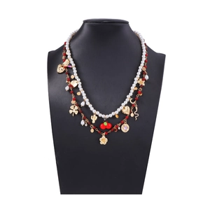 Detail of layered necklace with white pearls, red beads, and gold floral pendants