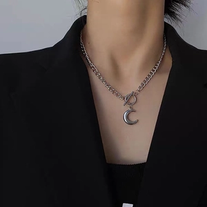 Collana con ciondolo a mezzaluna d'argento e chiusura OT indossata su una giacca nera