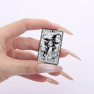 Tarot style enamel brooch with witch and black cat design held by hand on white background