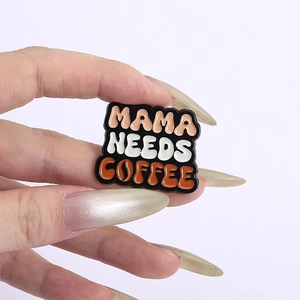 Detail of hand-held enamel pin with the motivational phrase Mama Needs Coffee in colorful text